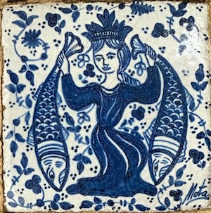 Ceramic tile with cobalt blue painting, depicting a crowned woman in medieval-ish dress, holding 2 fishes by their tails. The signature says 'Mota'.